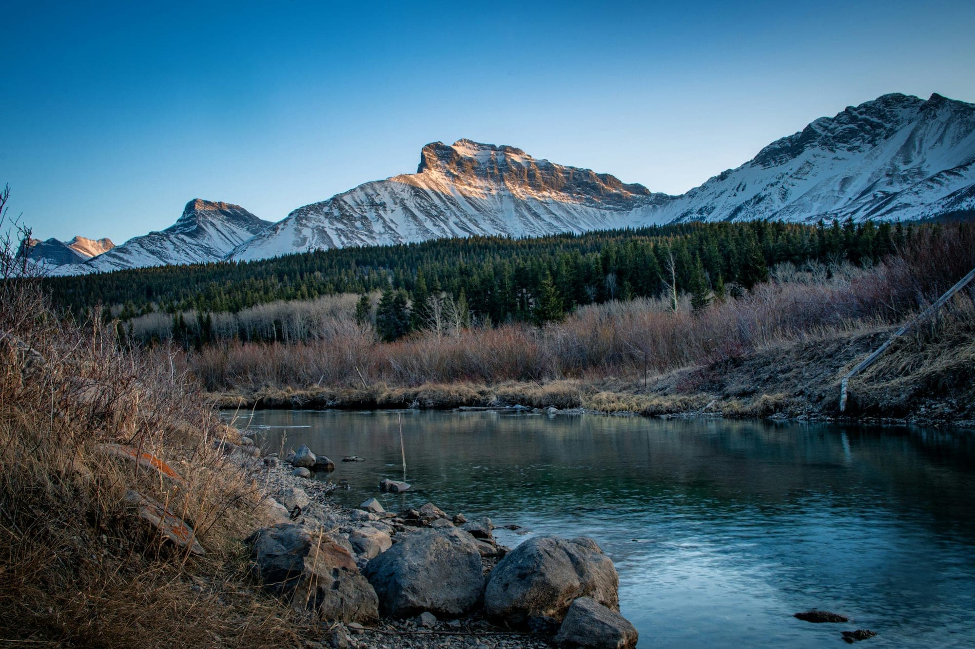 Early morning on a river in the Crowsnest Pass, snow-capped peaks catching the first light